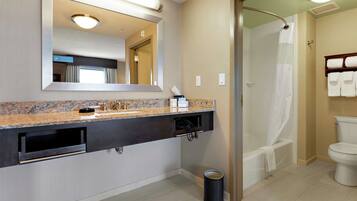 Un baño moderno con encimera de granito, un espejo grande, una ducha con puerta de vidrio y un inodoro.