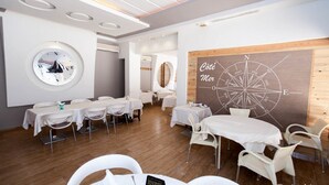 A modern dining area with round tables and white chairs, a large compass wall art, and a sailboat image on the wall. - City Business Monastir Center (Monastir)