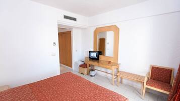 Un dormitorio con una cama, un escritorio con una computadora, una silla y un espejo.