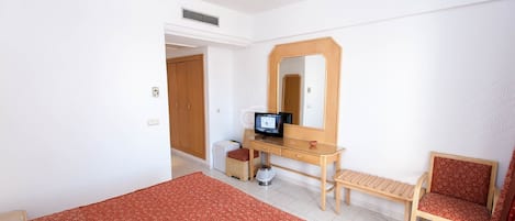 A bedroom with a bed, a desk with a computer, a chair, and a mirror.