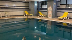 An indoor swimming pool with clear water, yellow lounge chairs, and a tiled floor. - City Business Monastir Center (Monastir)