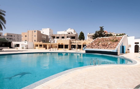 Una piscina al aire libre, sombrillas, sillones reclinables de piscina