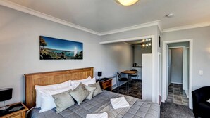 A bedroom with a bed, bedside table, and a painting of a coastal scene. - Admiral Motel (Christchurch)