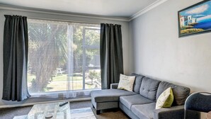 A living room with a grey sofa, a glass coffee table, and a painting on the wall. - Admiral Motel (Christchurch)