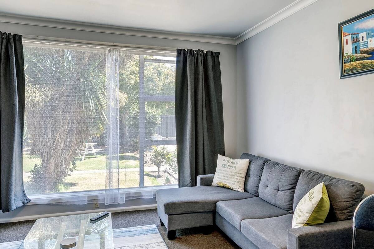 A living room with a grey sofa, a glass coffee table, and a painting on the wall.
