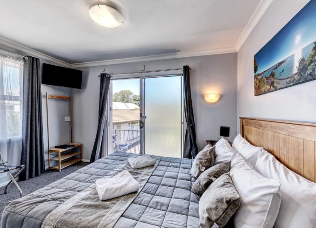 A hotel room with a bed, a TV, a balcony, and a painting on the wall.