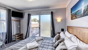 Una habitación de hotel con cama, televisor, balcón y un cuadro en la pared.