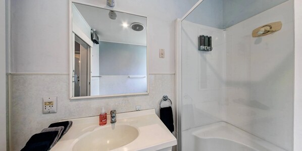 A bathroom with a white sink, a mirror, a towel rack, and a shower area.