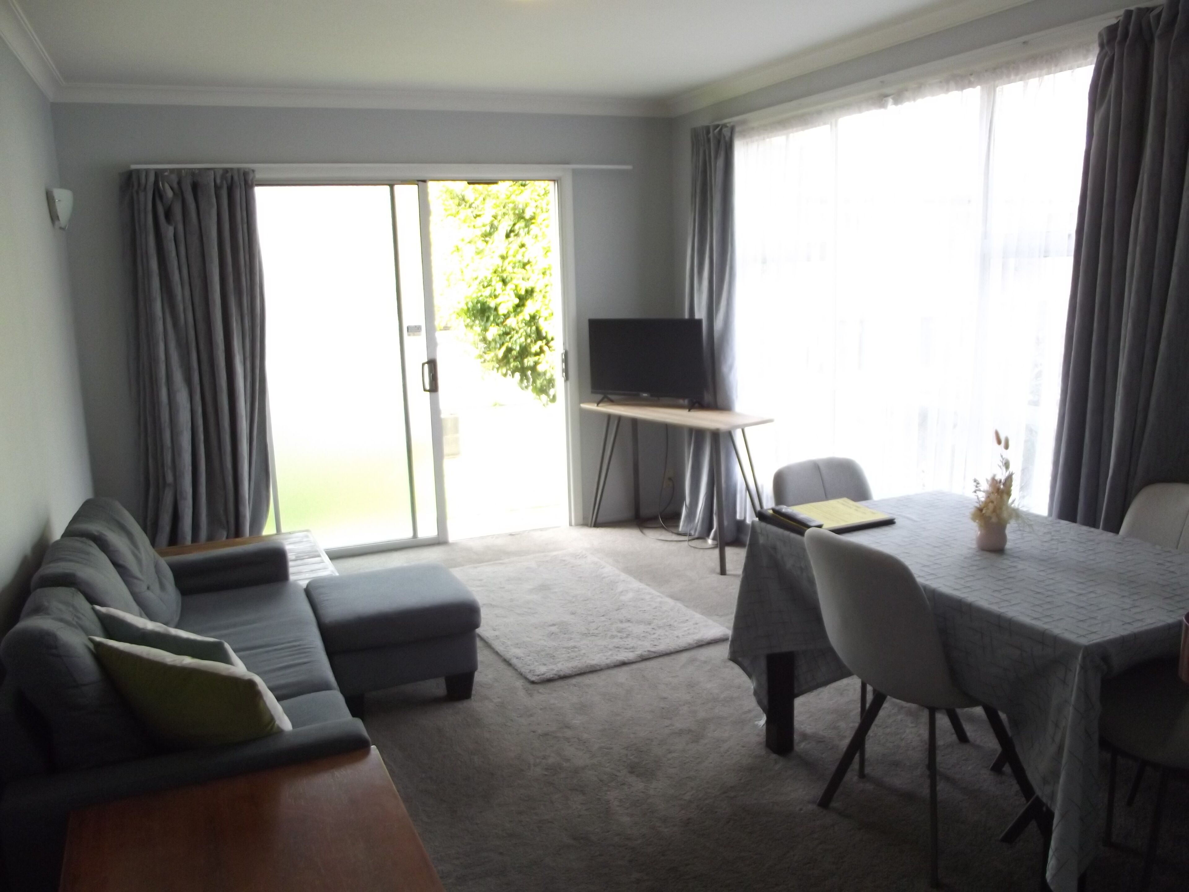 A living room with a sofa, ottoman, TV, and dining table with chairs.