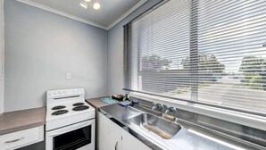 A kitchen with a stove, oven, sink, and window with blinds. - Admiral Motel (Christchurch)