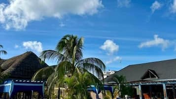 Una piscina con sillones de descanso y palmeras, rodeada de edificios con diseño tropical.