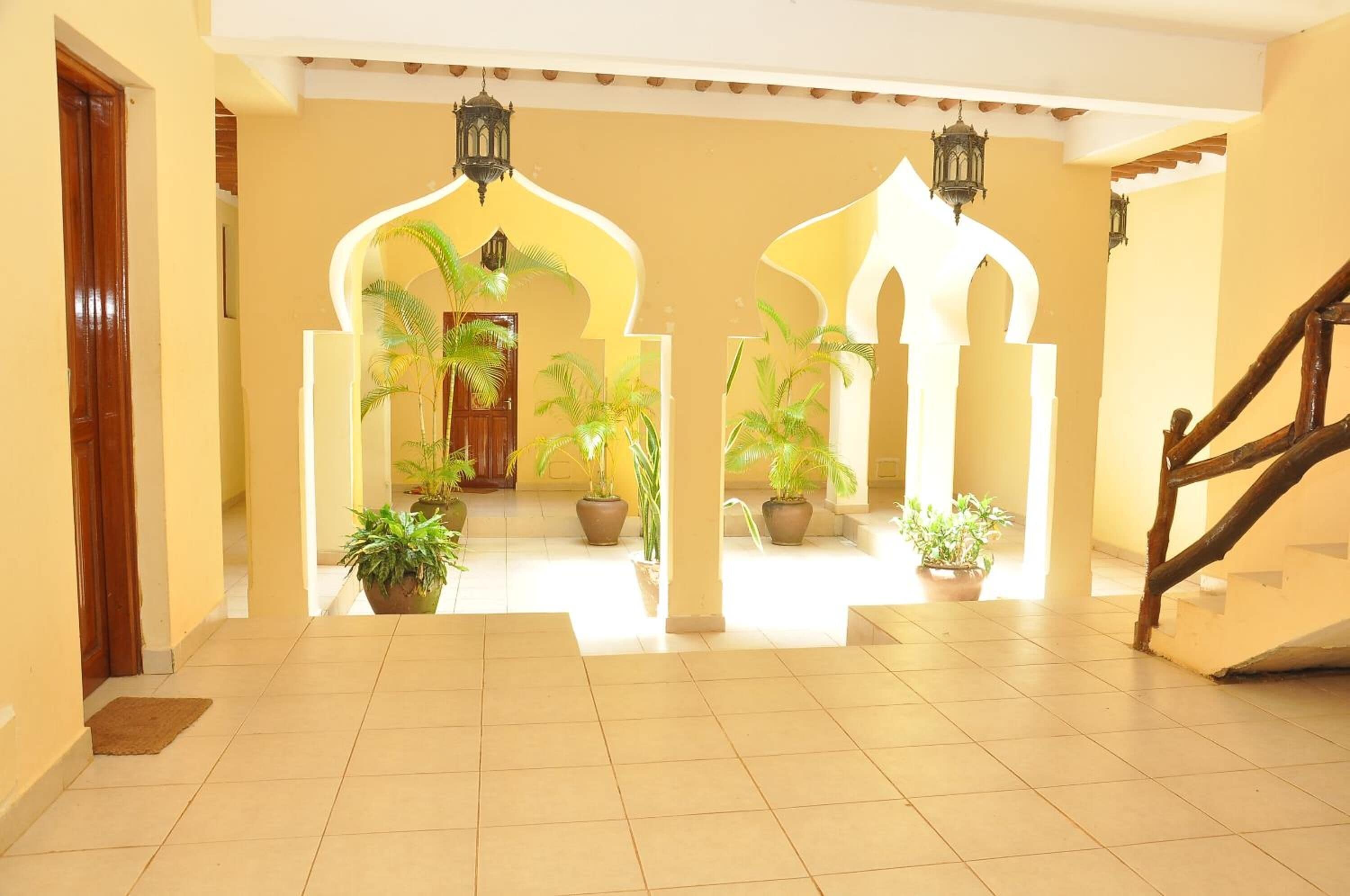 A hallway with tiled flooring, potted plants, and a wooden staircase.