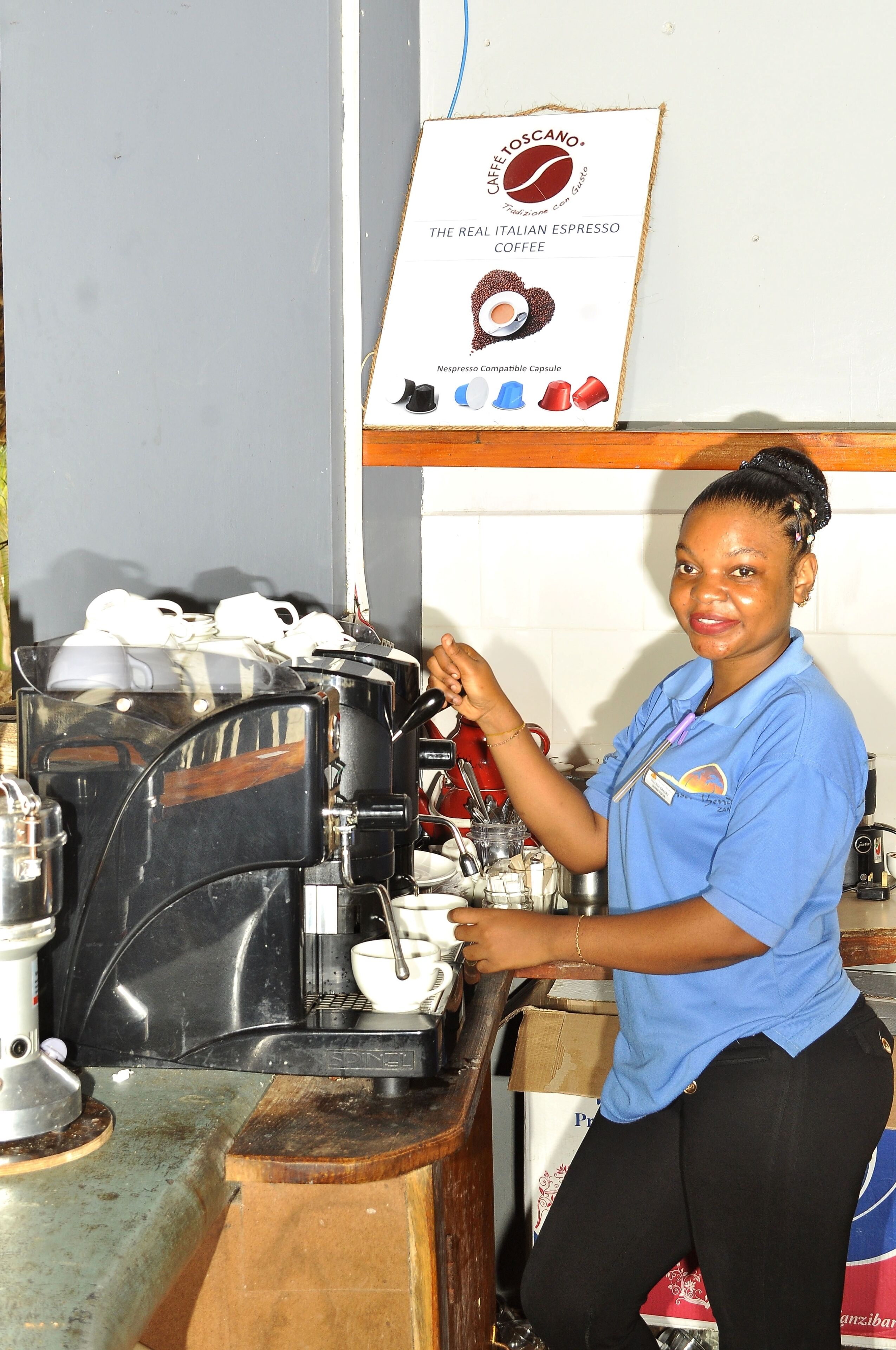 A person operating a coffee machine in a kitchen area with a coffee cup and a sign about Italian espresso.