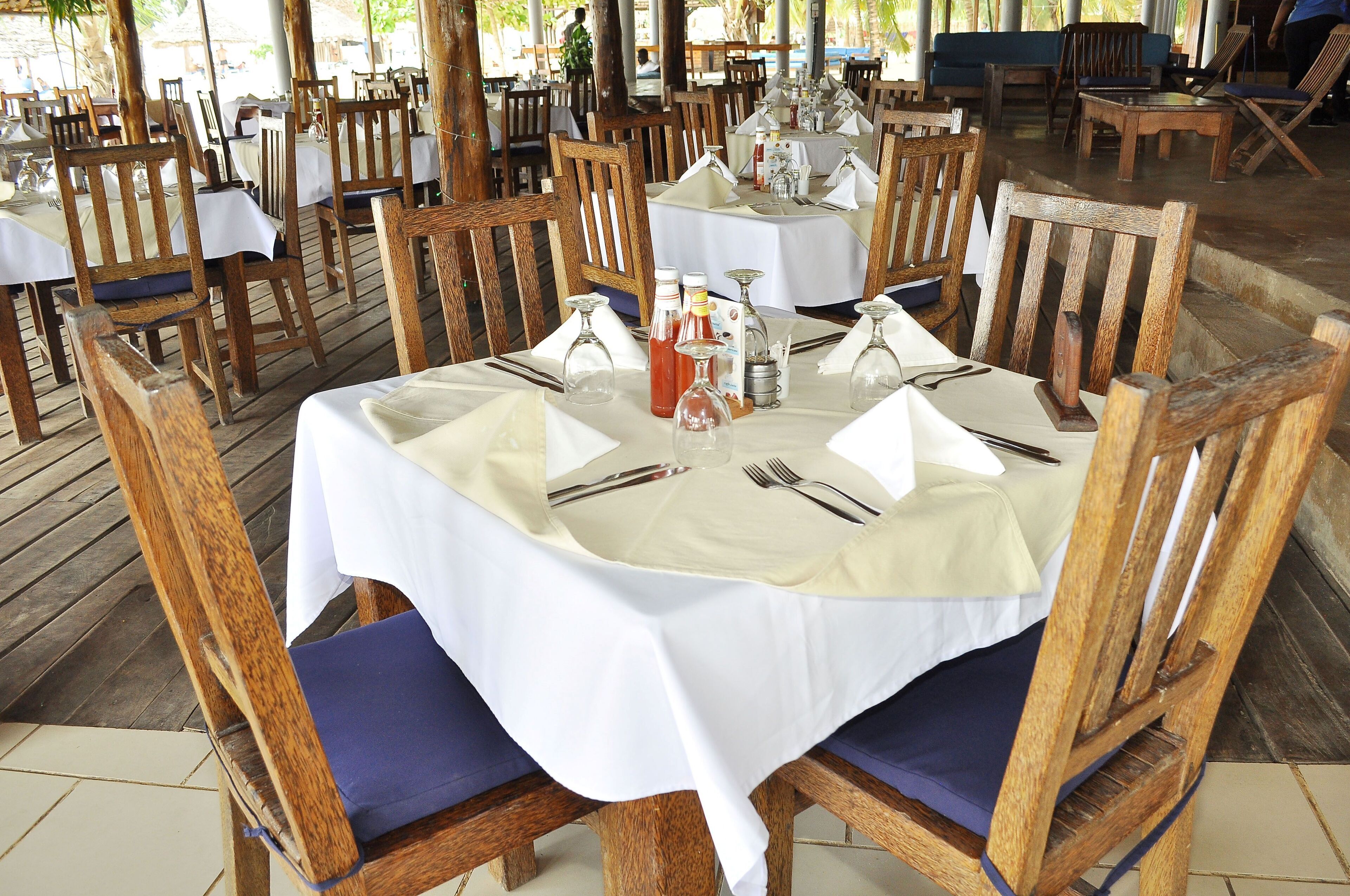 Un restaurant avec des chaises et des tables en bois, chaque table étant dressée avec une nappe blanche, des verres et des couverts.