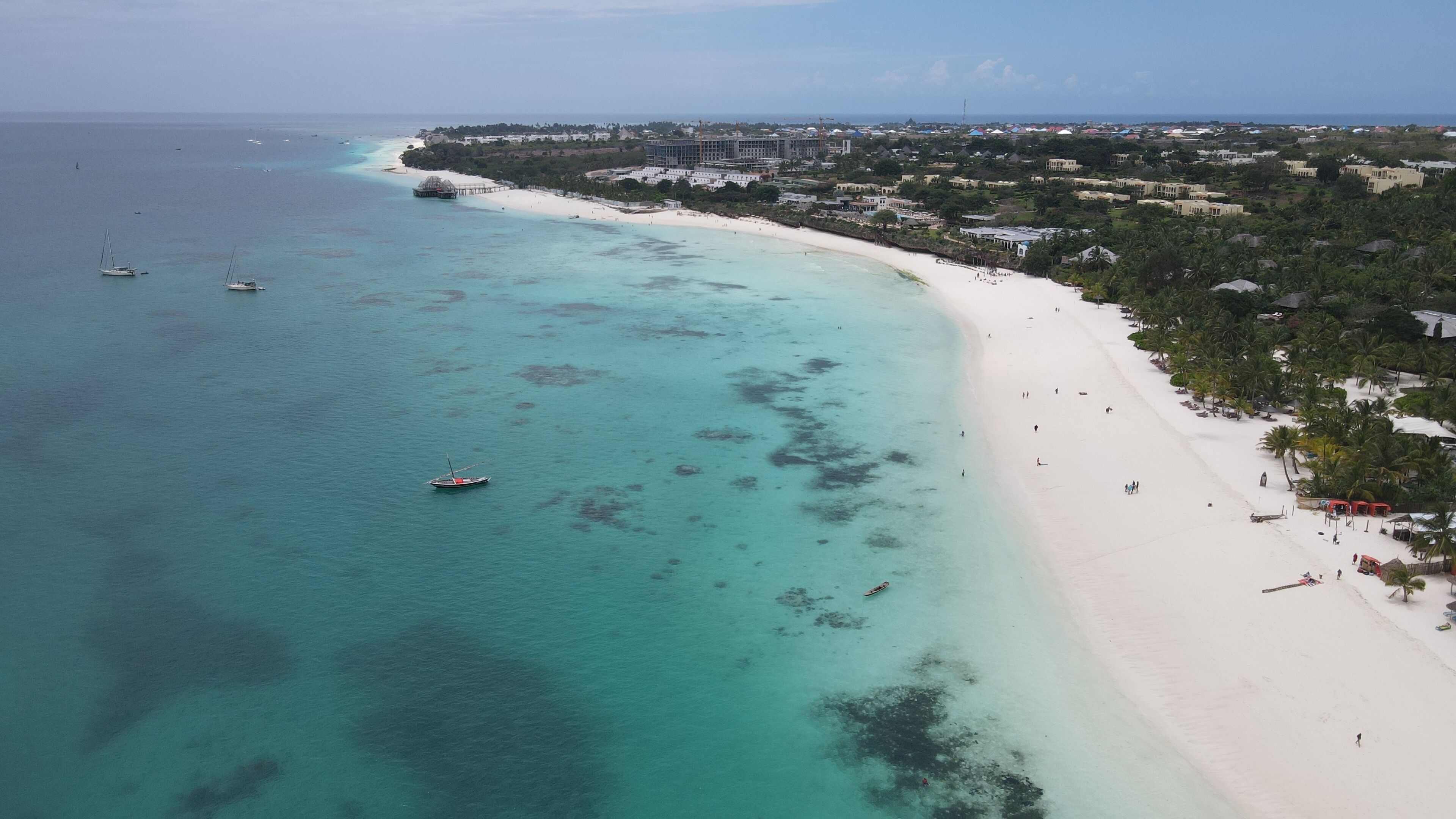 A coastal area with a sandy beach, clear turquoise waters, and a few boats.