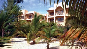 Un resort con edificios de varios pisos, palmeras y suelo arenoso.