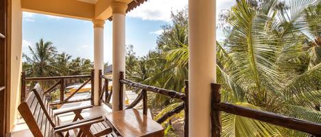 A covered outdoor seating area with wooden benches and a view of palm trees.