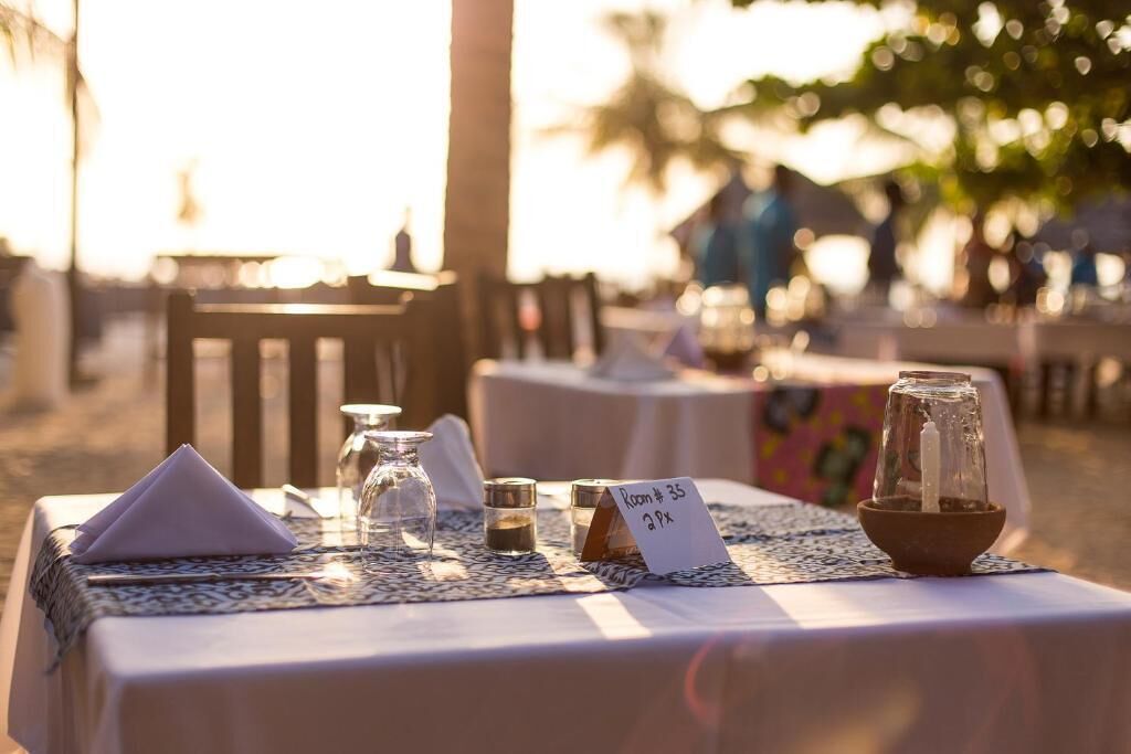 A table set for dining outdoors with a placemat, napkin, salt and pepper shakers, a candle holder, and a sign indicating room number and price.
