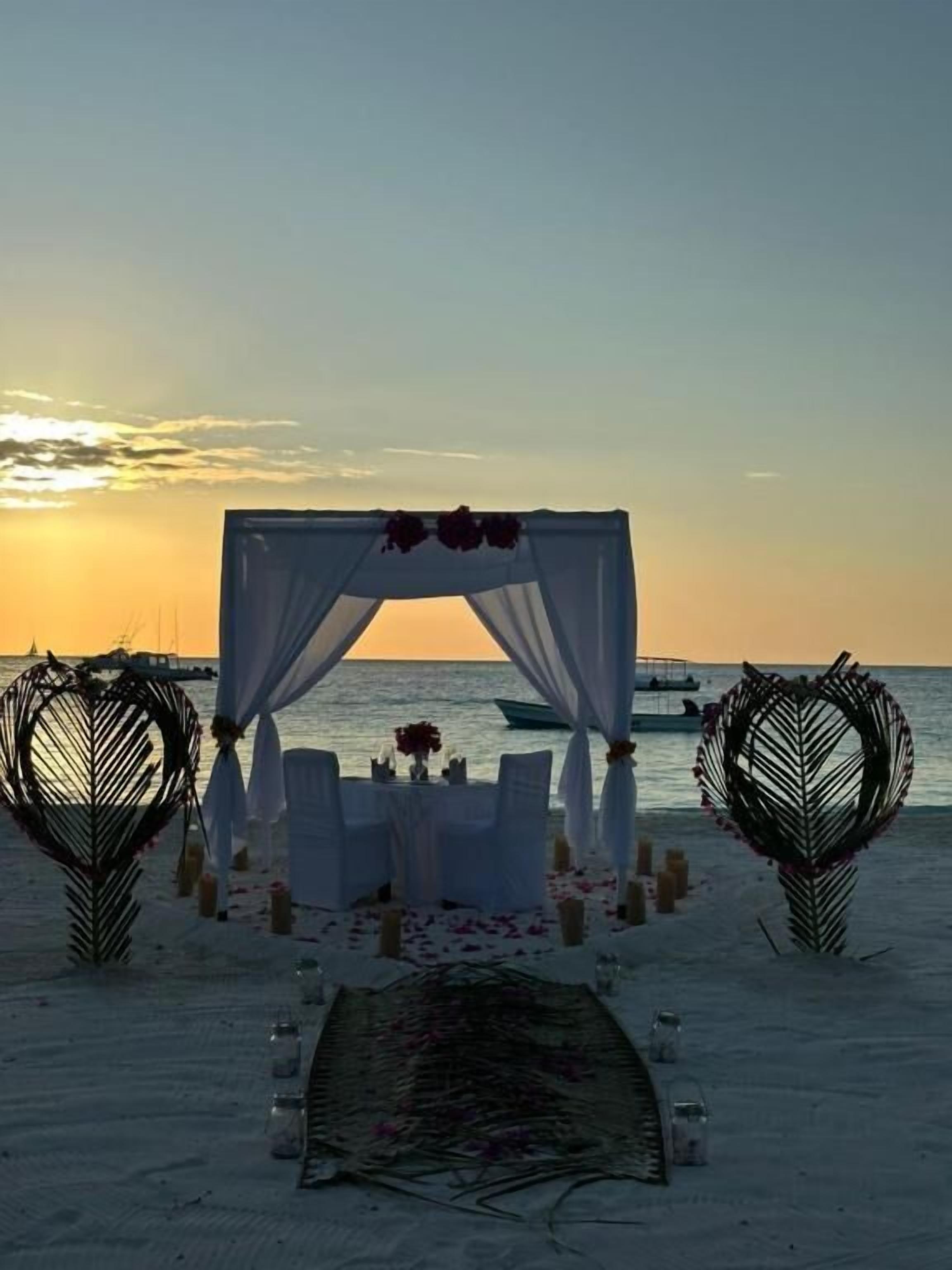 Une cérémonie de mariage organisée sur la plage, avec un dais blanc, des tables et des chaises, ainsi que des éléments de décoration en forme de cœur.