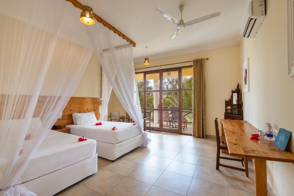 Une chambre d’hôtel avec deux lits, un balcon, une table à manger et un ventilateur de plafond.