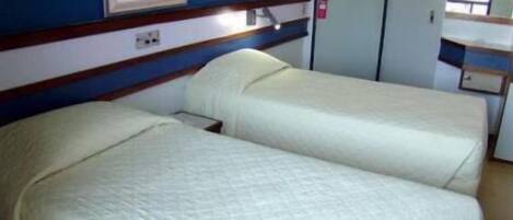Una habitación estándar de hotel con dos camas individuales, una mesita de noche pequeña y un armario.