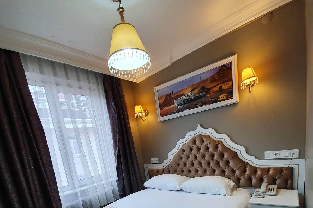 Ett hotellrum med en stor säng, en kristallkrona, en tavla på väggen och ett nattduksbord med en telefon.