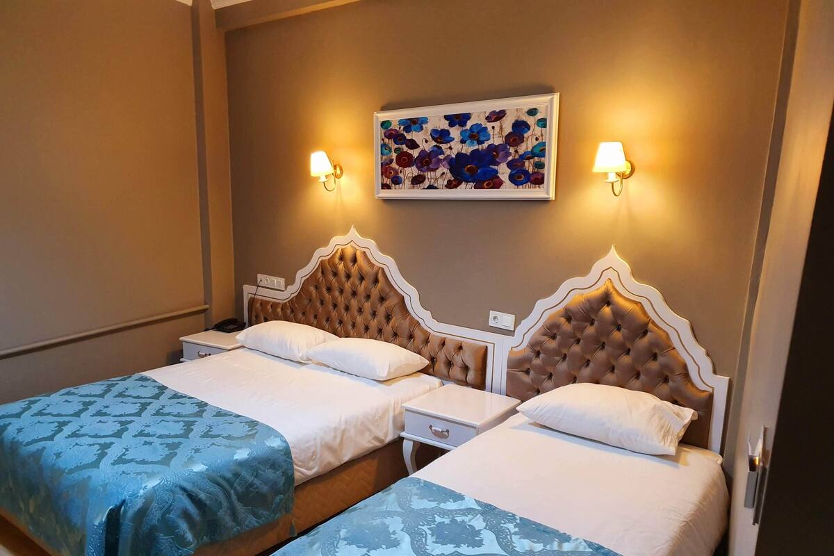 Ett hotellrum med två sängar, var och en med ett stoppat sänggavell, vita sängbord och ett inramat blomstermotiv ovanför sängarna.