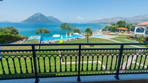 A view of a pool area with a mountain in the background, a fenced balcony, and a building with a red roof. - Thesmos Village (Xiromero)
