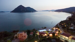 A coastal view with a mountain, calm sea, and a lit residential area with houses and a small building. - Thesmos Village (Xiromero)