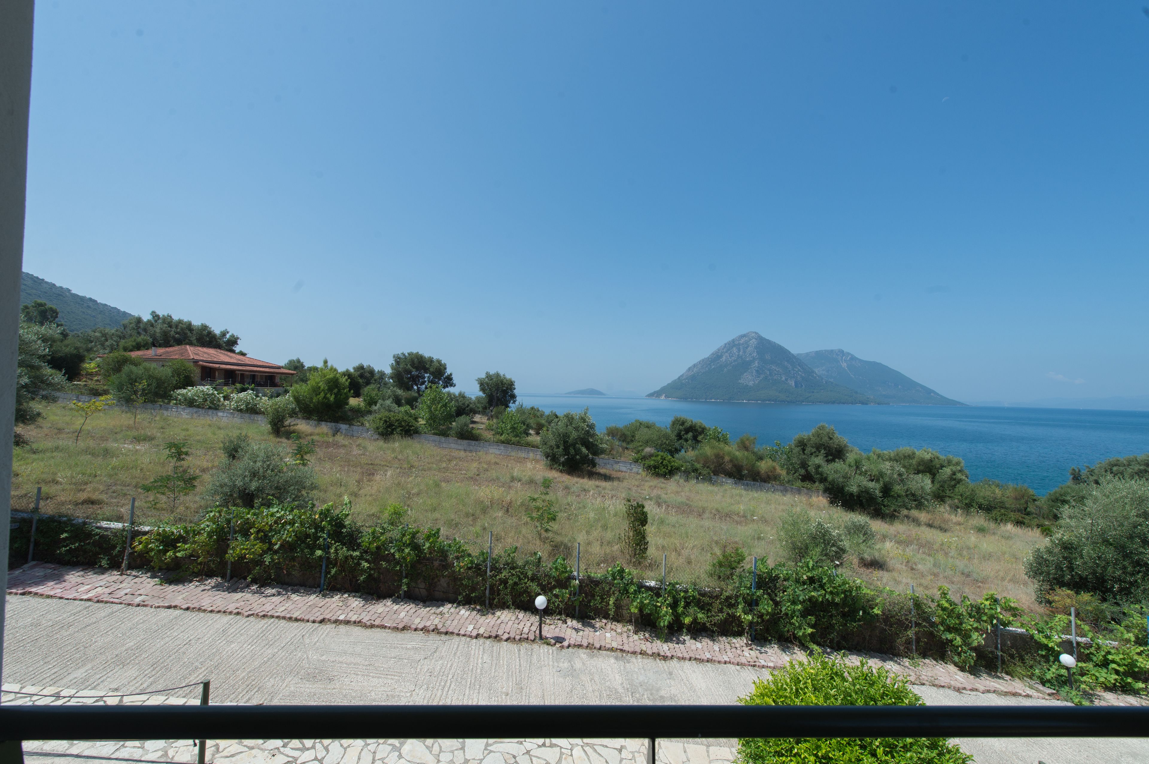 Paesaggio costiero con una casa, vegetazione e una montagna sullo sfondo.