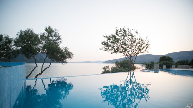 A clear view of an infinity pool with a reflection of trees and mountains in the water. - Thesmos Village (Xiromero)