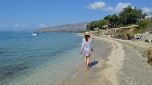 A beach with clear water, a woman walking, and a boat in the distance. - Thesmos Village (Xiromero)