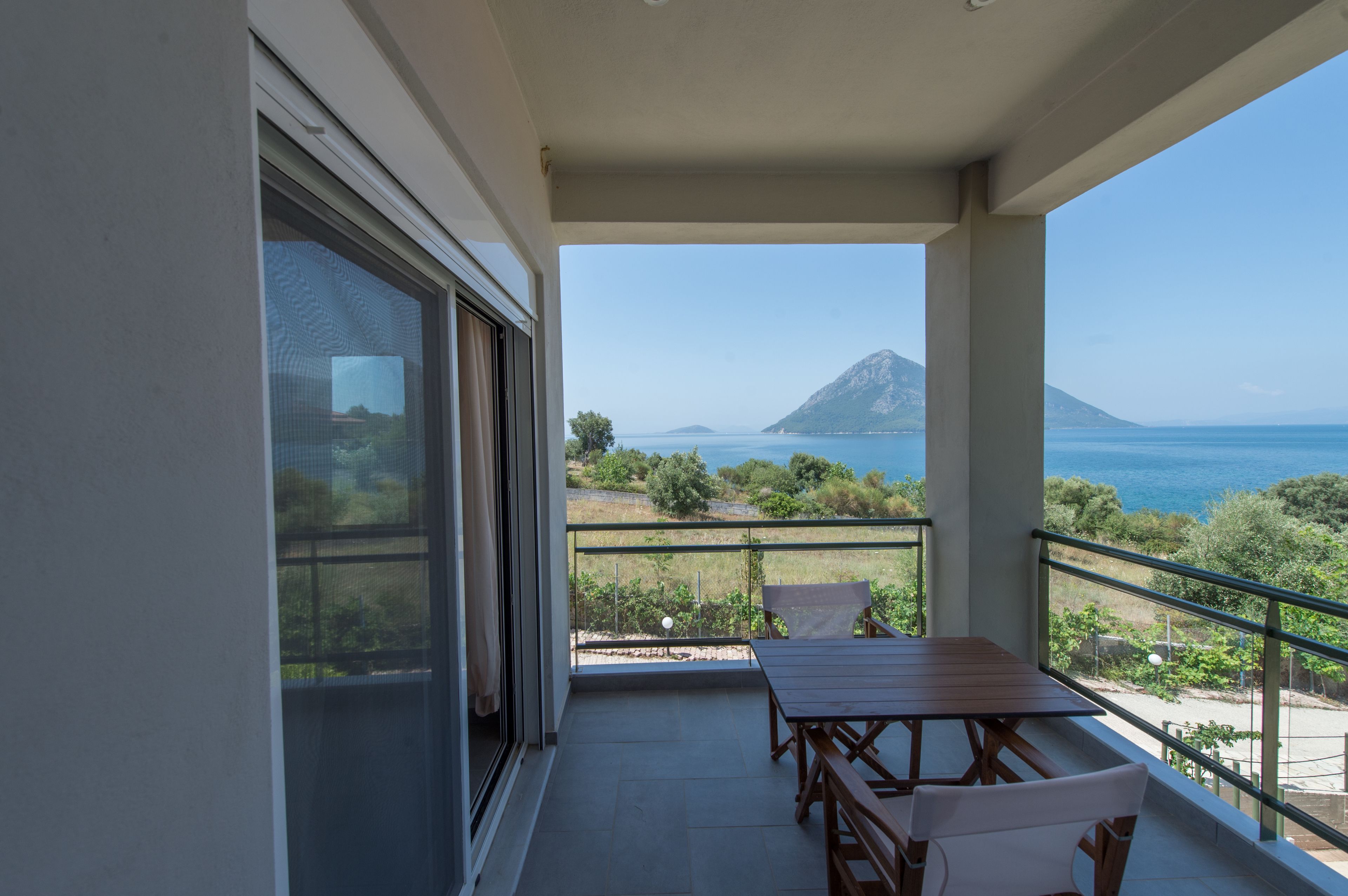 Uma varanda com mesa e cadeiras, com vista para o mar e uma montanha.