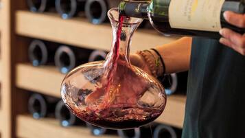 A person pouring wine into a glass, with a wine rack in the background.