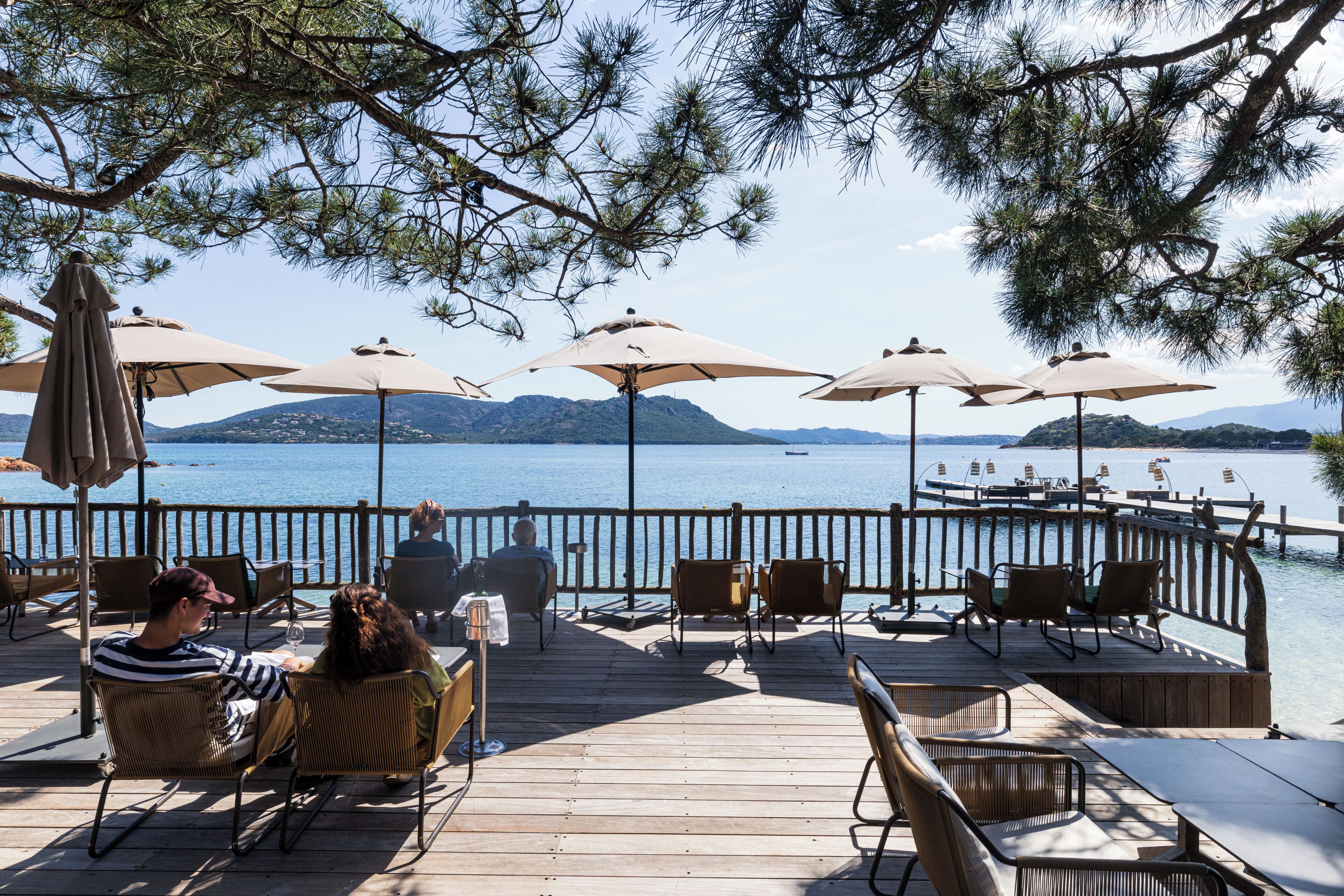 Une terrasse en bois avec des sièges d’extérieur, des parasols et une vue sur un lac et des montagnes.