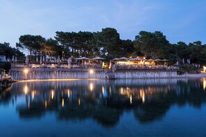 Una propiedad frente al agua con zonas de estar al aire libre, un muelle y su reflejo en el agua.