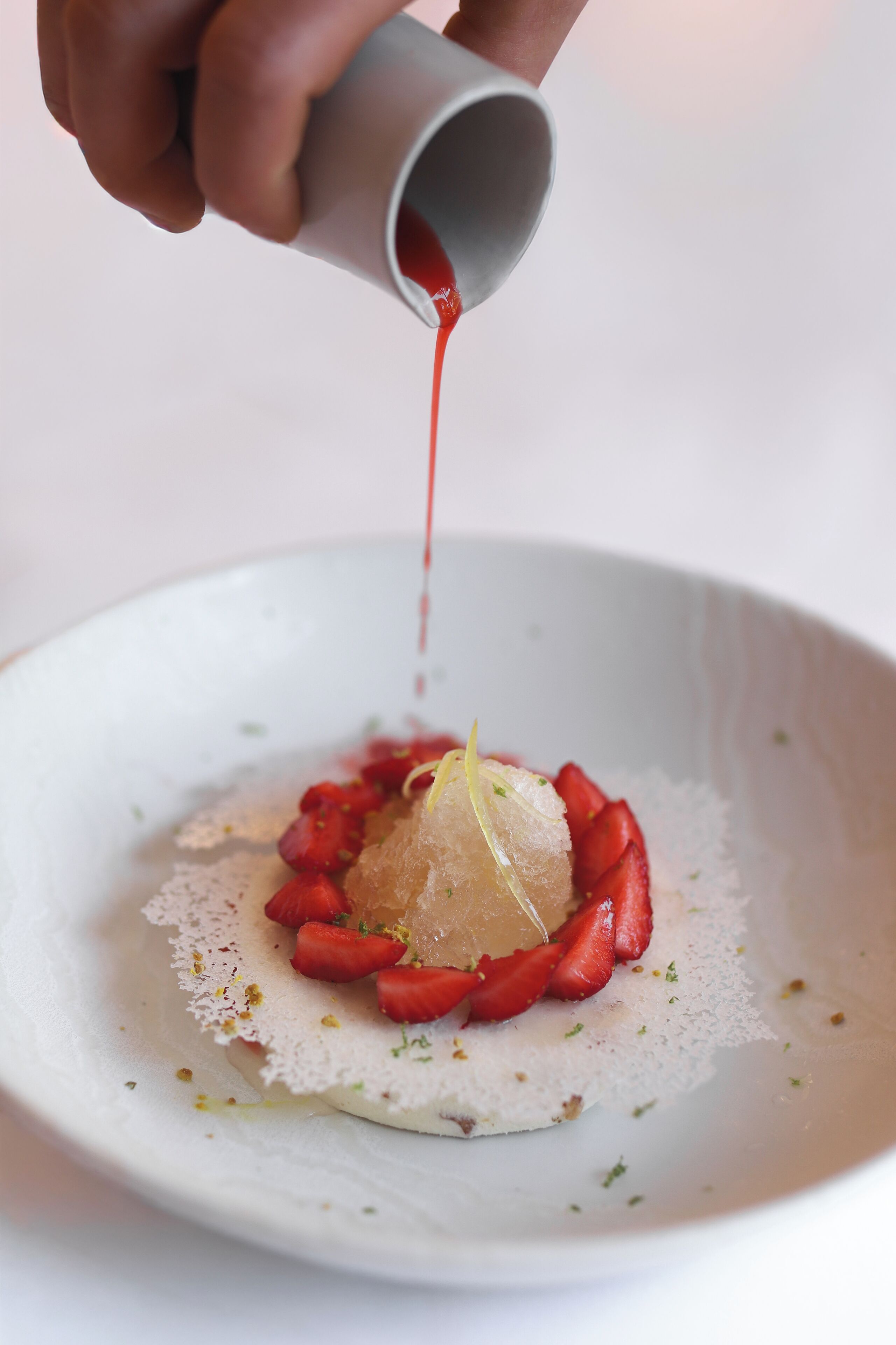 A hand pouring a red liquid into a white bowl containing a food item.