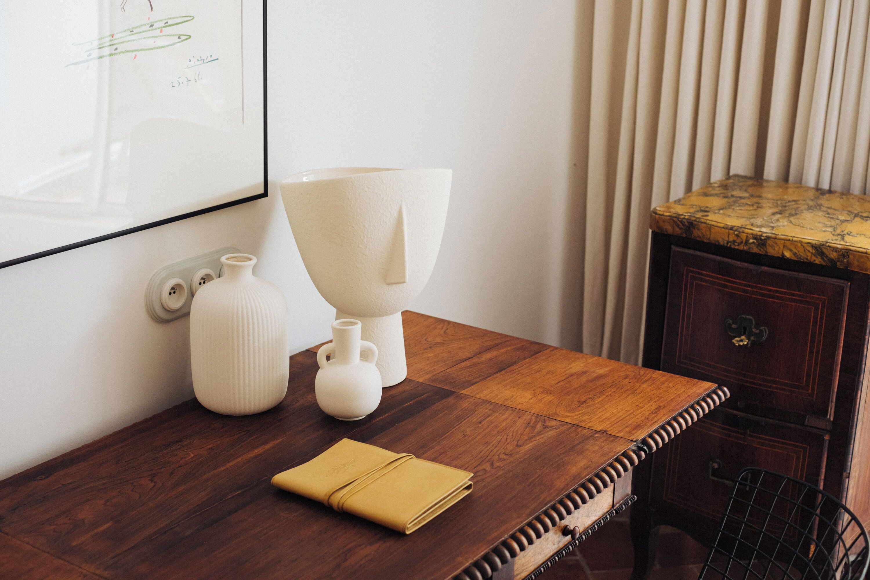 A wooden table with white vases, a folded towel, and a framed picture on the wall.