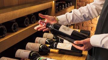 A person selecting a wine bottle from a wooden wine rack in a brick-walled room.
