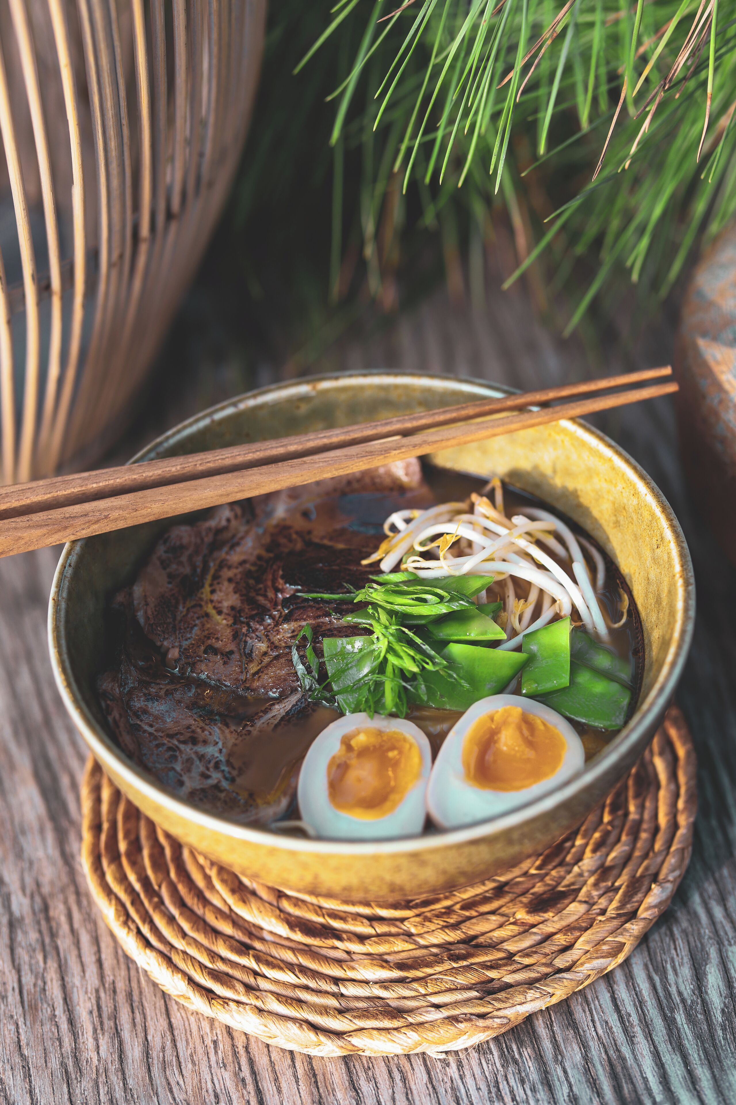 A bowl of soup with noodles, meat, and vegetables, served on a woven mat.