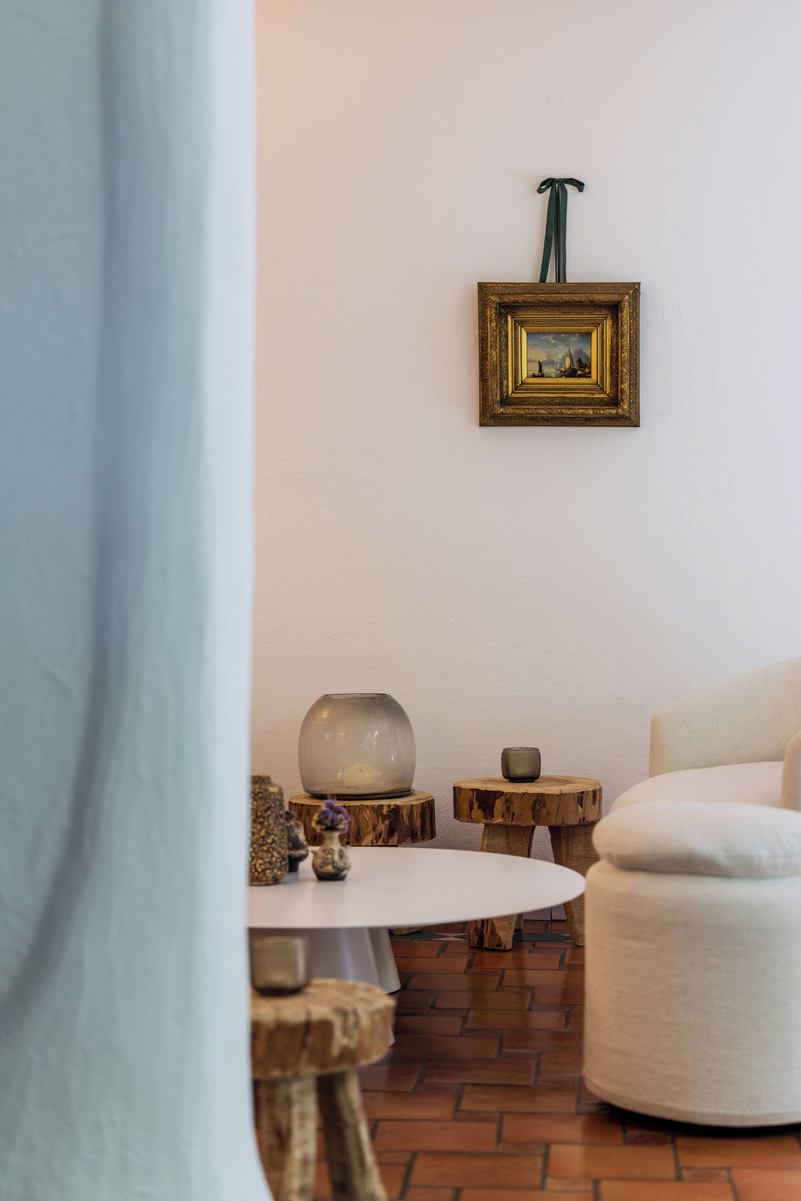 Une pièce avec une table ronde blanche, une chaise blanche, un petit tabouret en bois, un vase décoratif et un tableau encadré accroché au mur.