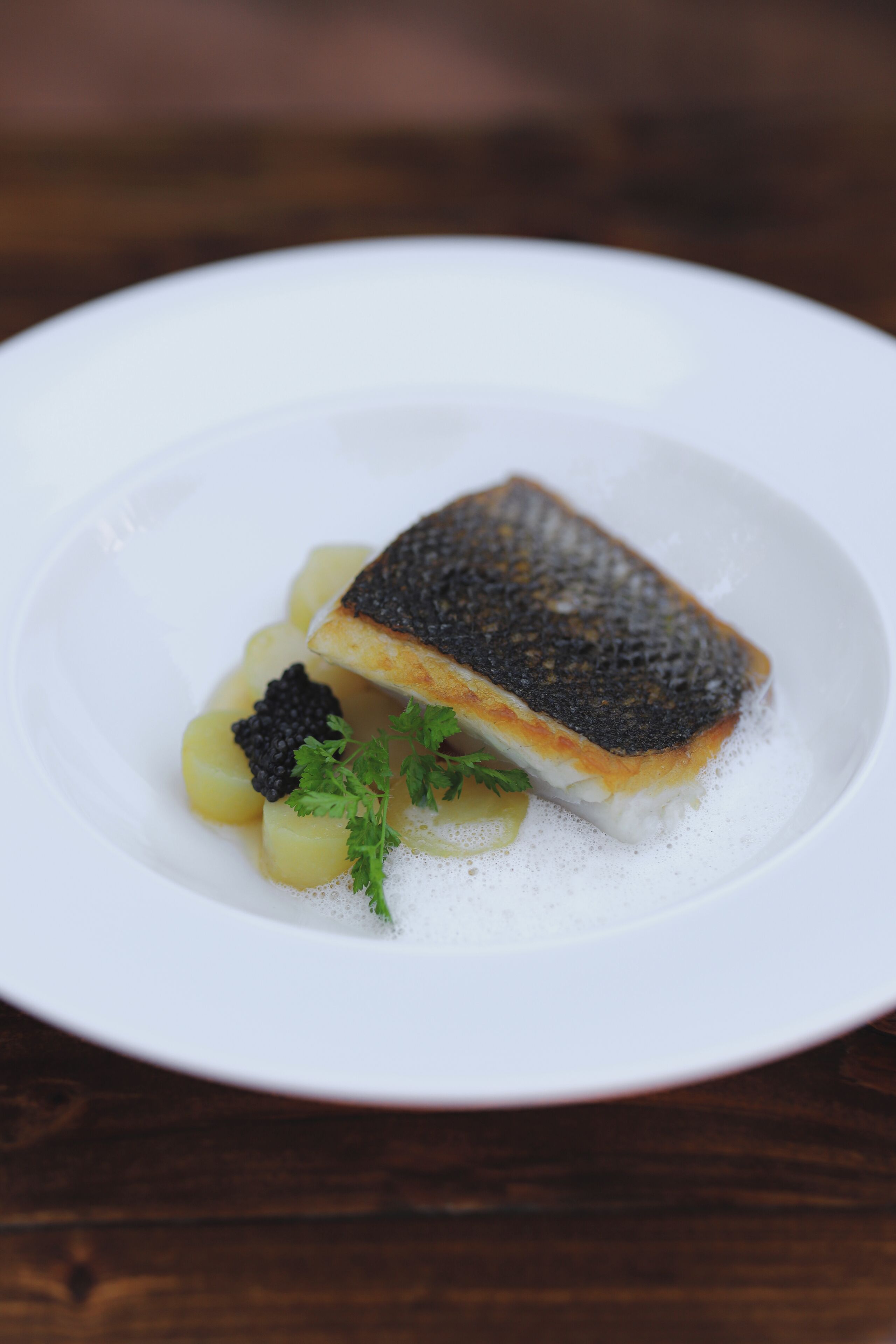 A white plate with a piece of fish, potatoes, and black caviar.