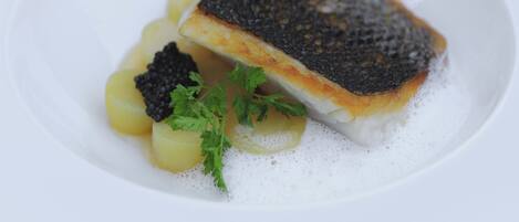 A white plate with a piece of fish, potatoes, and black caviar.