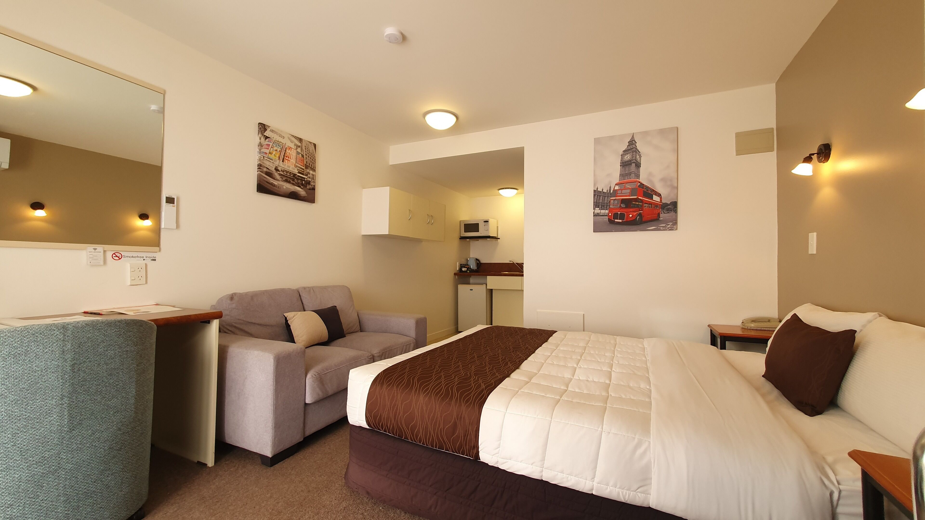 A hotel room with a bed, a desk, a sofa, a kitchenette, and a bathroom.