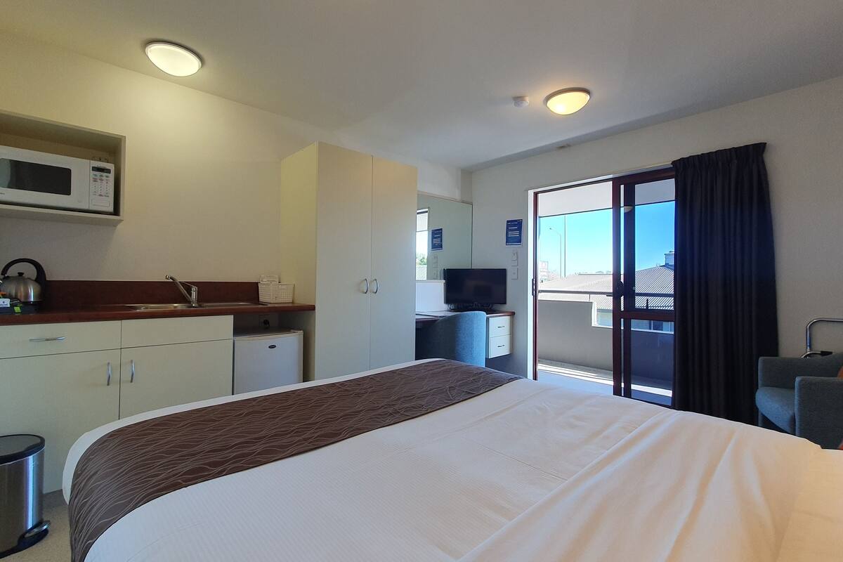 A hotel room with a bed, kitchenette, and a balcony with a view.