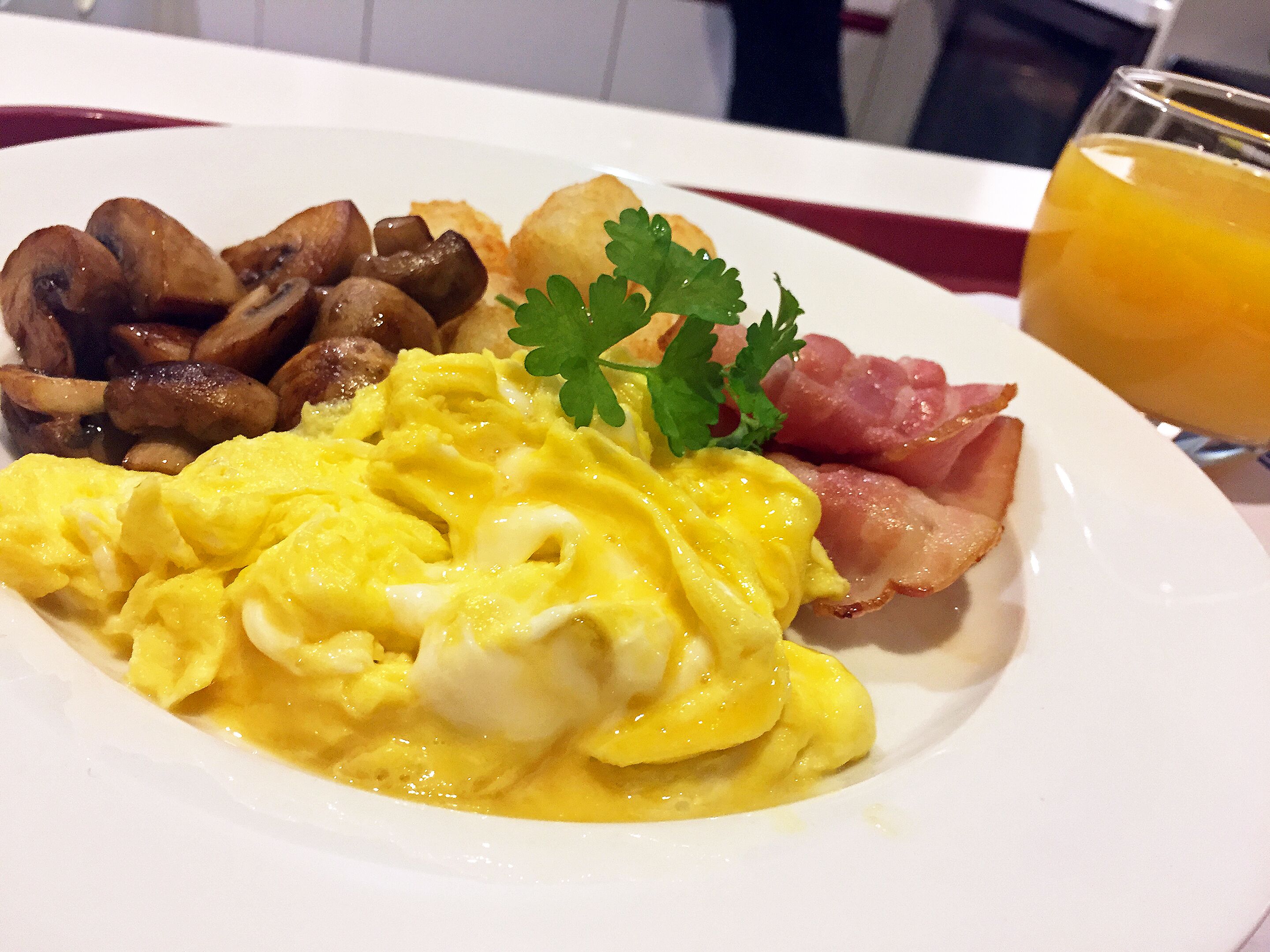 A breakfast plate with scrambled eggs, bacon, mushrooms, and a glass of orange juice.