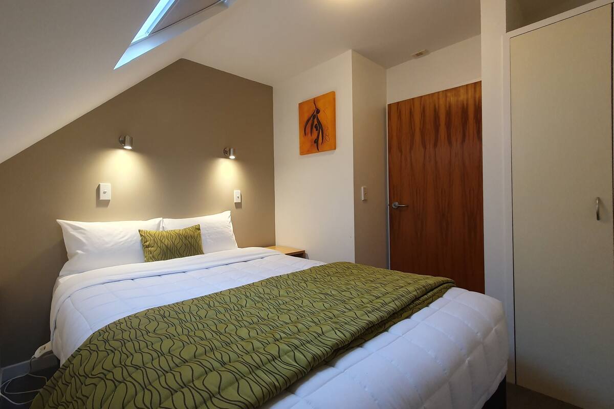 A bedroom with a bed, a wooden wardrobe, and a painting on the wall.