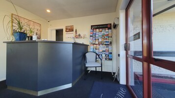 Zona de recepción con un mostrador de color oscuro, una silla, un panel informativo en la pared y una puerta de cristal que da al exterior.