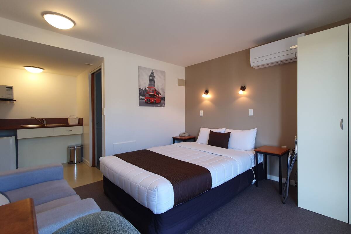 A hotel room with a bed, bedside table, wardrobe, and a kitchenette area.
