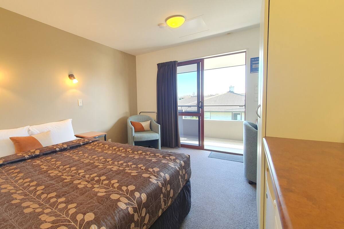 A hotel room with a large bed, two wall-mounted lights, a chair, and a balcony with a view.